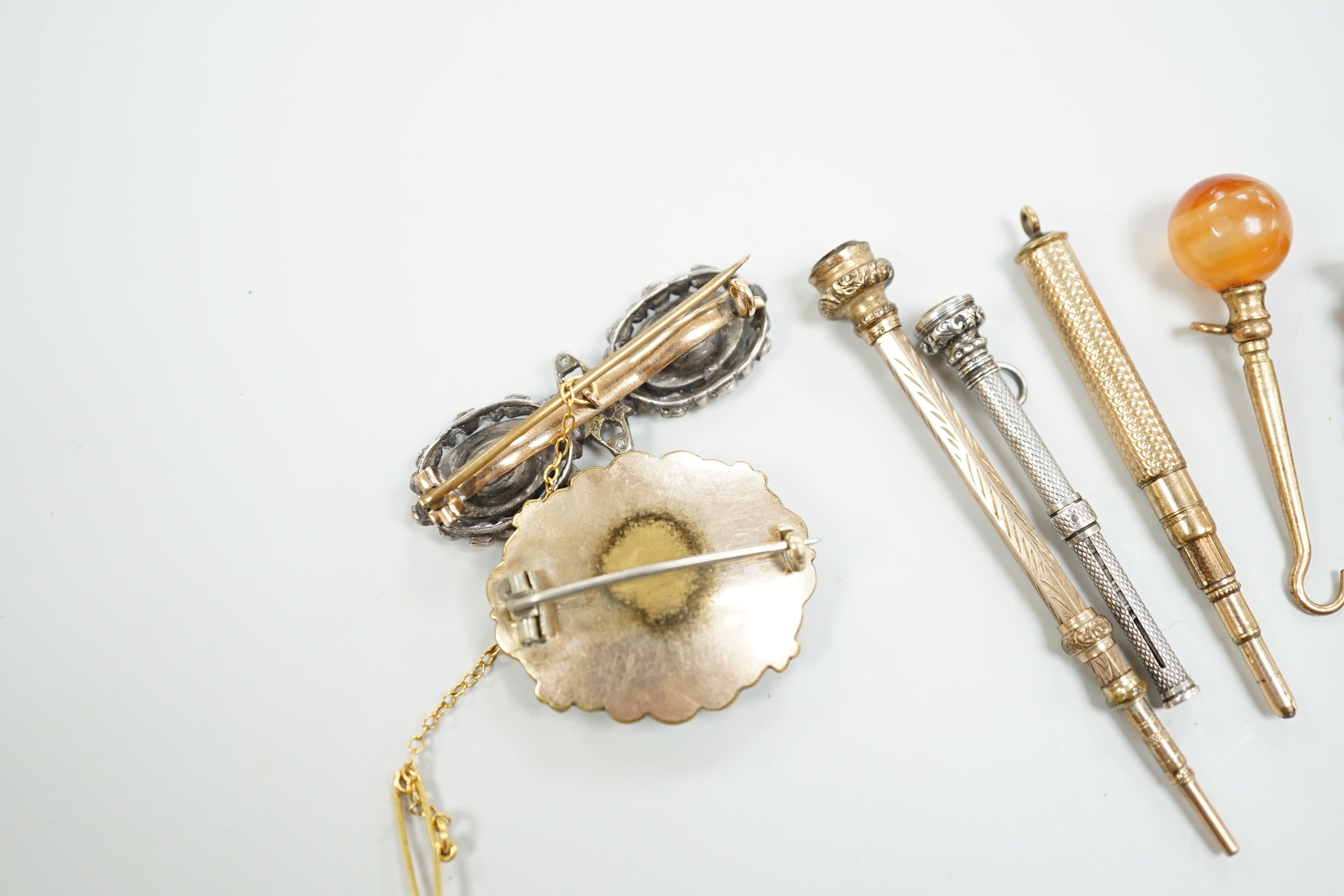 Four assorted early 20th century yellow or white metal overlaid propelling pencils, an agate set button hook, a two colour paste brooch and a Victorian enamelled mourning brooch, with plaited hair.